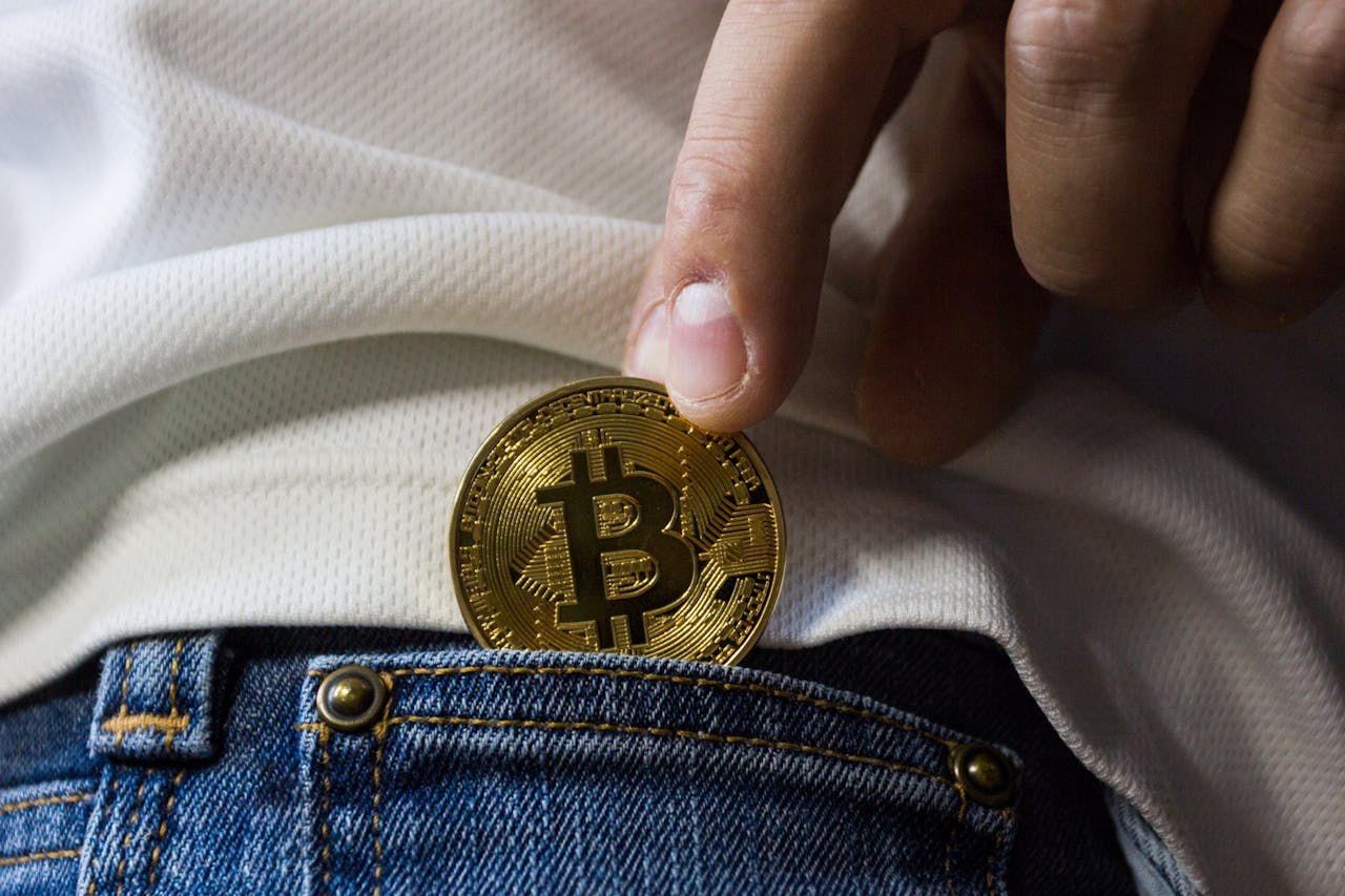 expertise-01 Close-up of hand putting Bitcoin in jeans pocket symbolizing cryptocurrency savings.